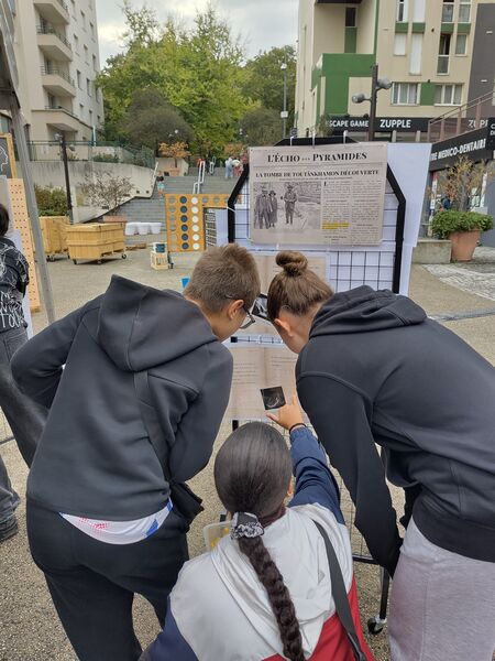 Des joueurs observent les documents affichés sur une grille du stand.